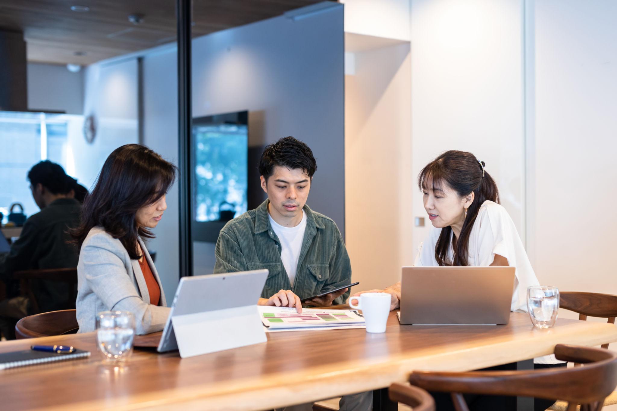 木製テーブルを囲み、3人で資料とタブレットを確認しながら打ち合わせをする様子