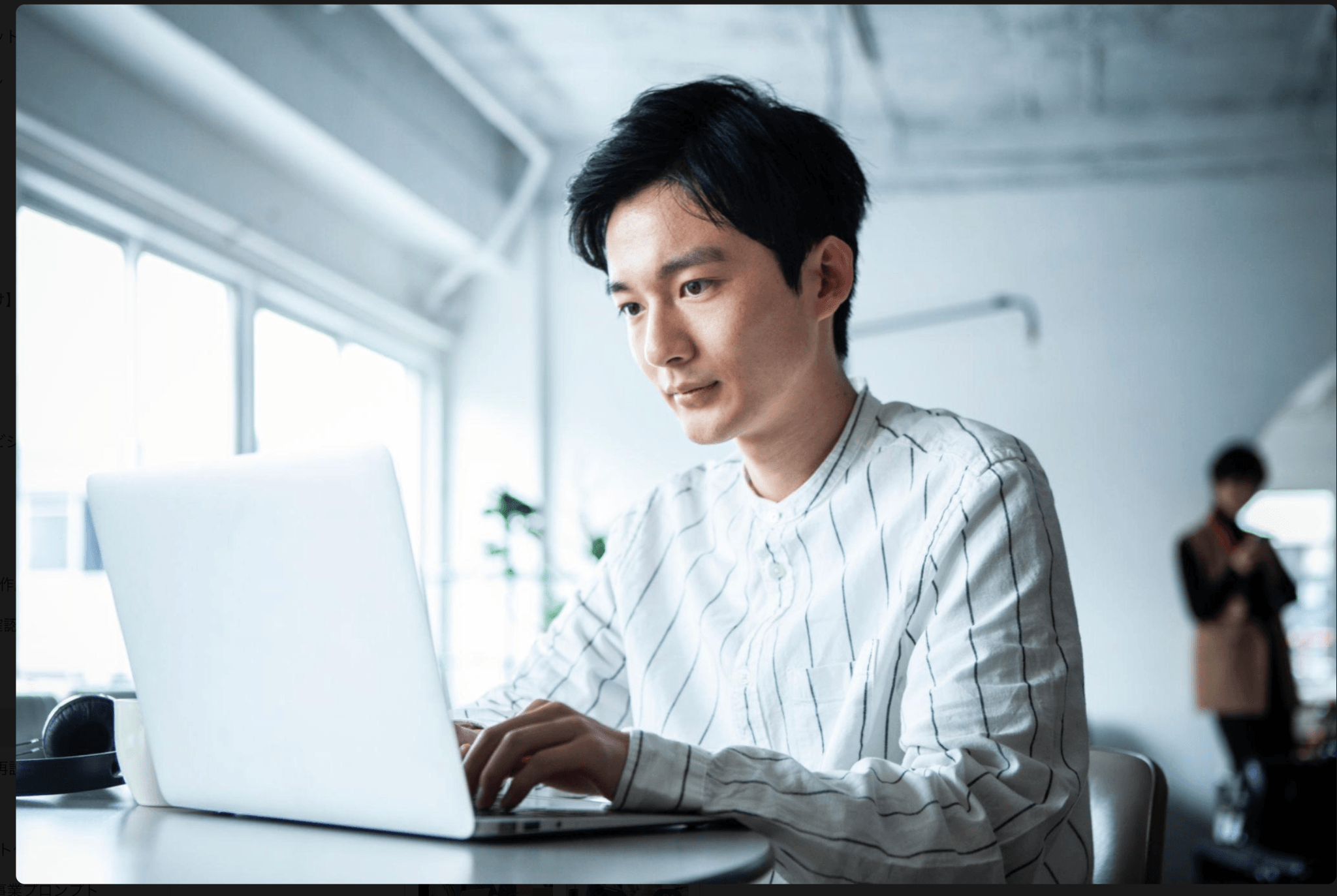 明るいオフィスで白いノートPCを操作するストライプシャツのビジネスパーソン